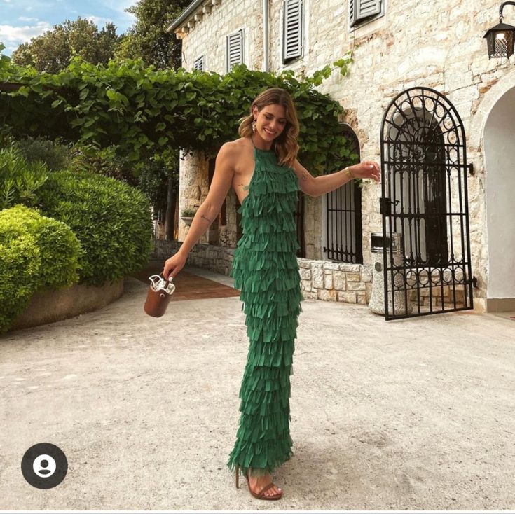 a woman standing in front of a stone building wearing a green dress with ruffles