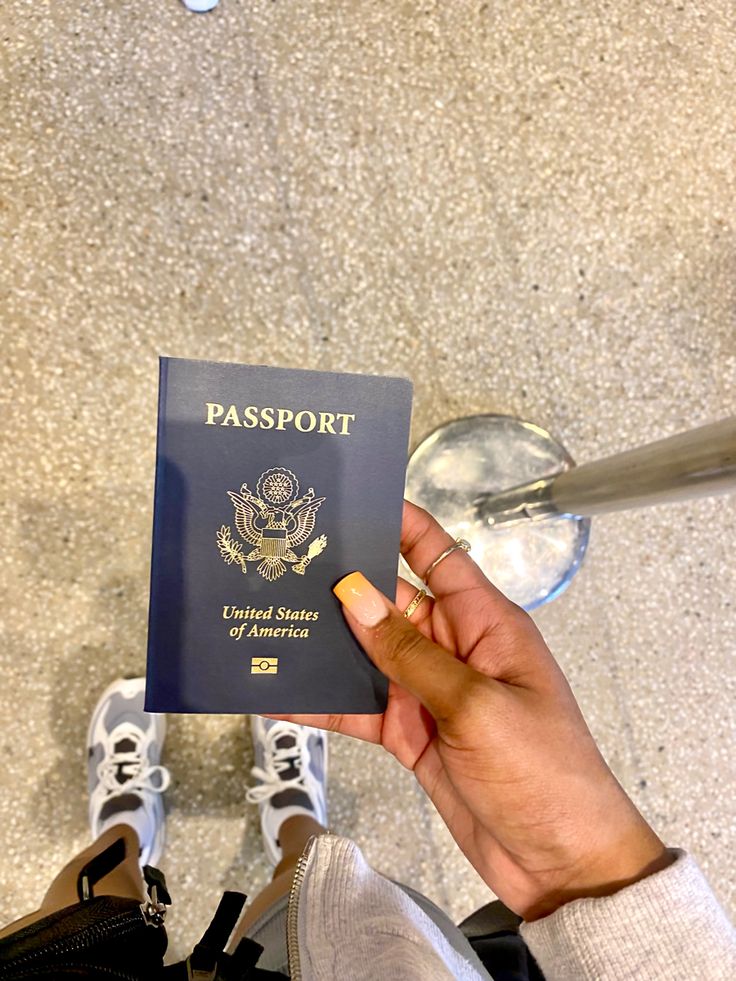 a person holding an american passport in their hand while standing next to a pair of shoes