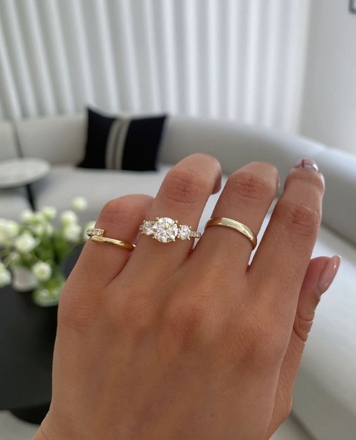 a woman's hand with two gold rings on it and a white couch in the background