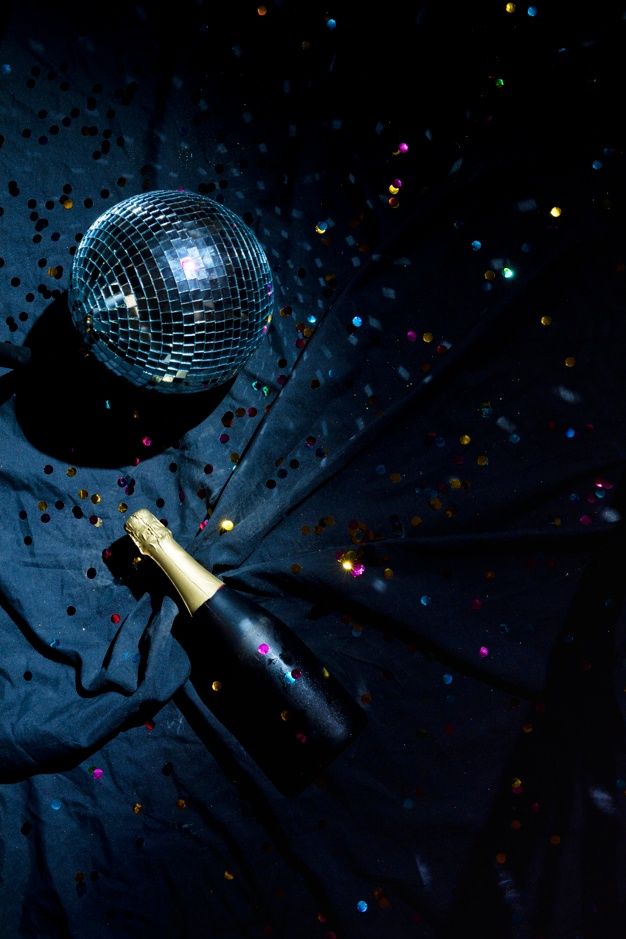 a bottle of champagne and a disco ball on a black background with confetti