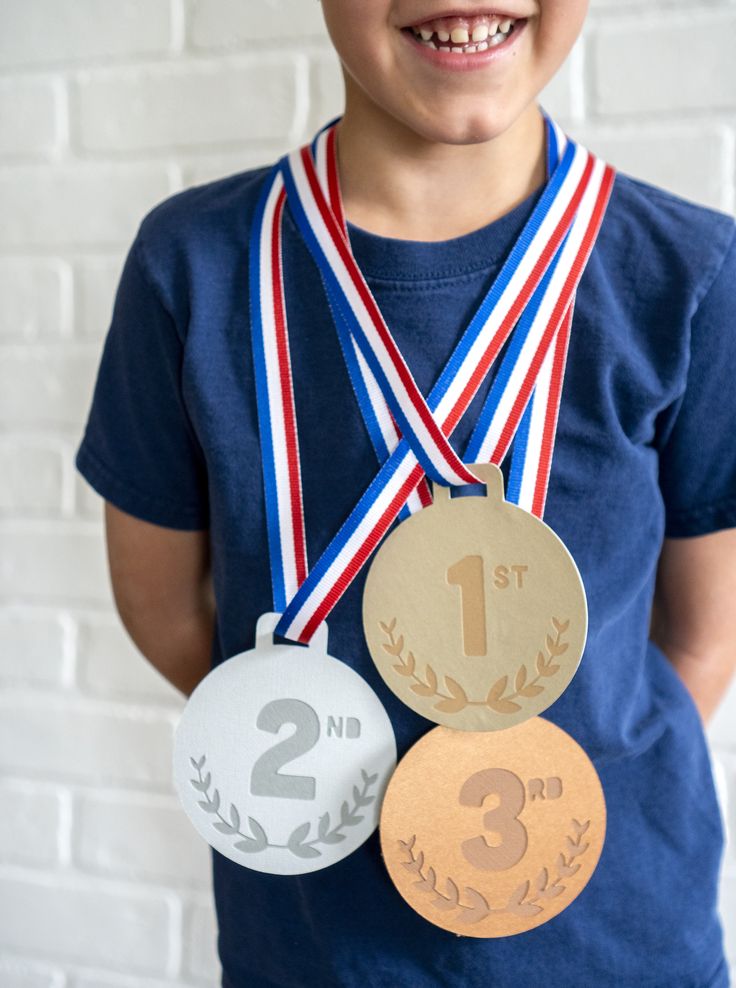 a young boy holding three medals in front of a white brick wall with the number one on it