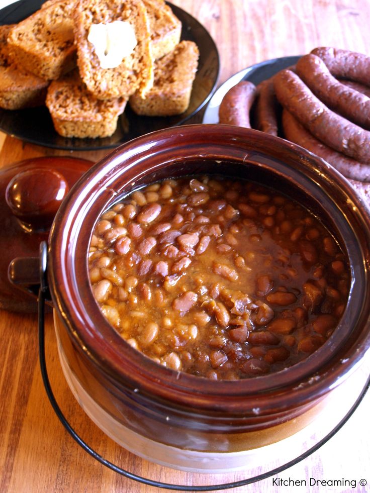 there is a bowl of beans next to bread and hotdogs on the table