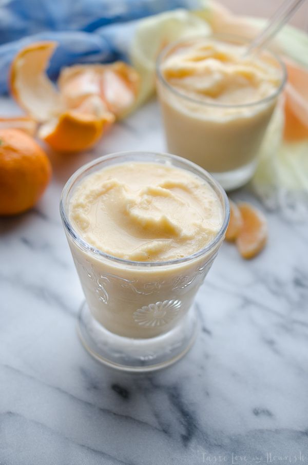 two small cups filled with cream sitting on top of a table next to oranges