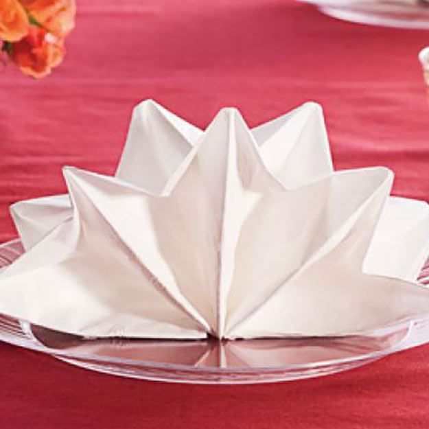 an origami flower on a glass plate at a table with flowers in the background