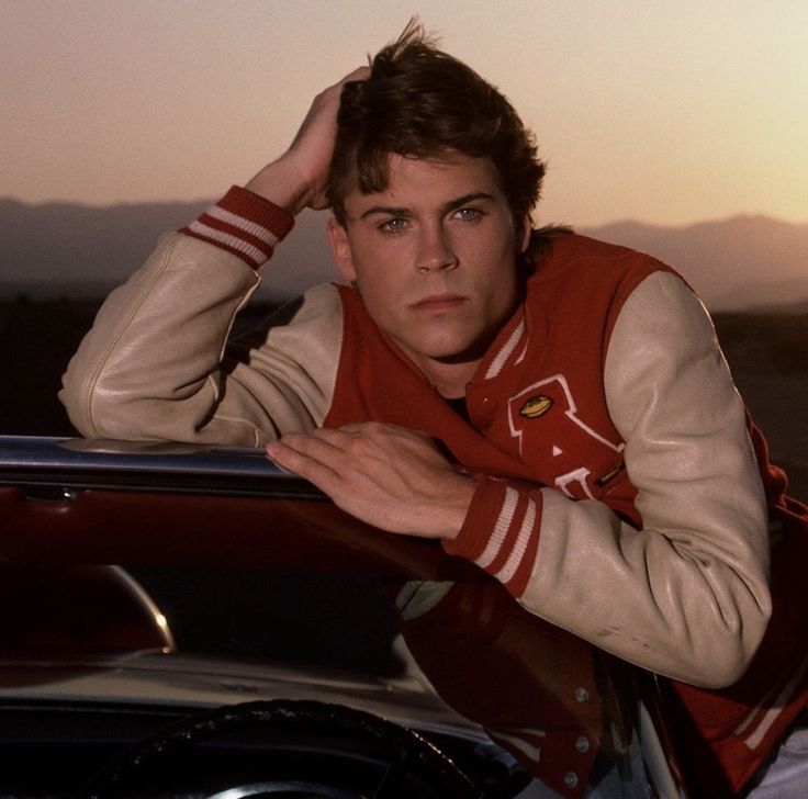 a young man leaning on the hood of a car with his hand on his head