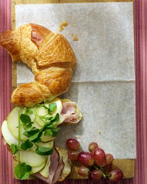 a croissant sandwich with meat, cheese and vegetables on it next to grapes