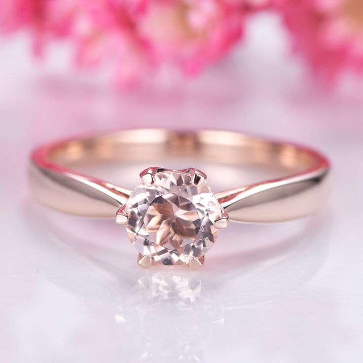 a close up view of a diamond ring on a white surface with pink flowers in the background