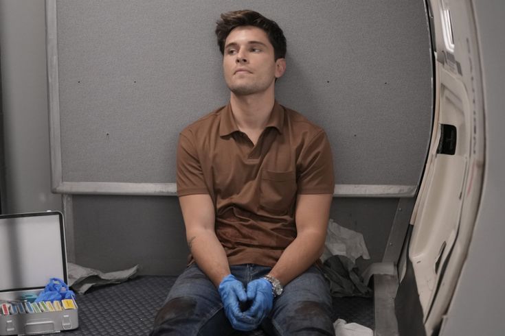 a man sitting on the floor in front of a refrigerator with blue gloves on his hands