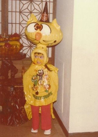 a child in a yellow cat costume standing next to a table with food on it