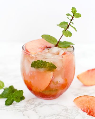 a glass filled with ice and mint garnish next to sliced peaches