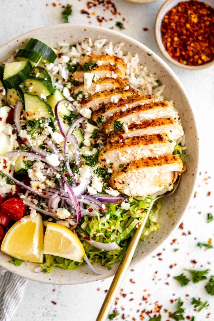 a white bowl filled with chicken, rice and veggies on top of a table