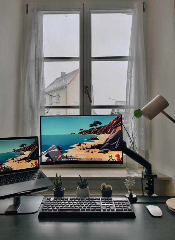 two laptops and a desktop computer on a desk in front of a large window