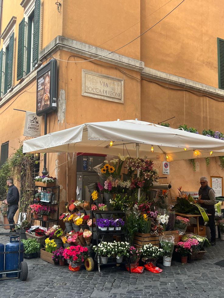 an open air market with flowers and plants on the side walk in front of a building