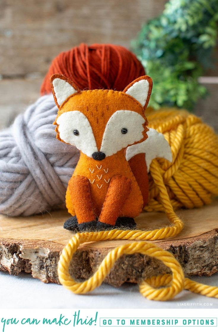 a red fox stuffed animal sitting on top of a piece of wood next to yarn