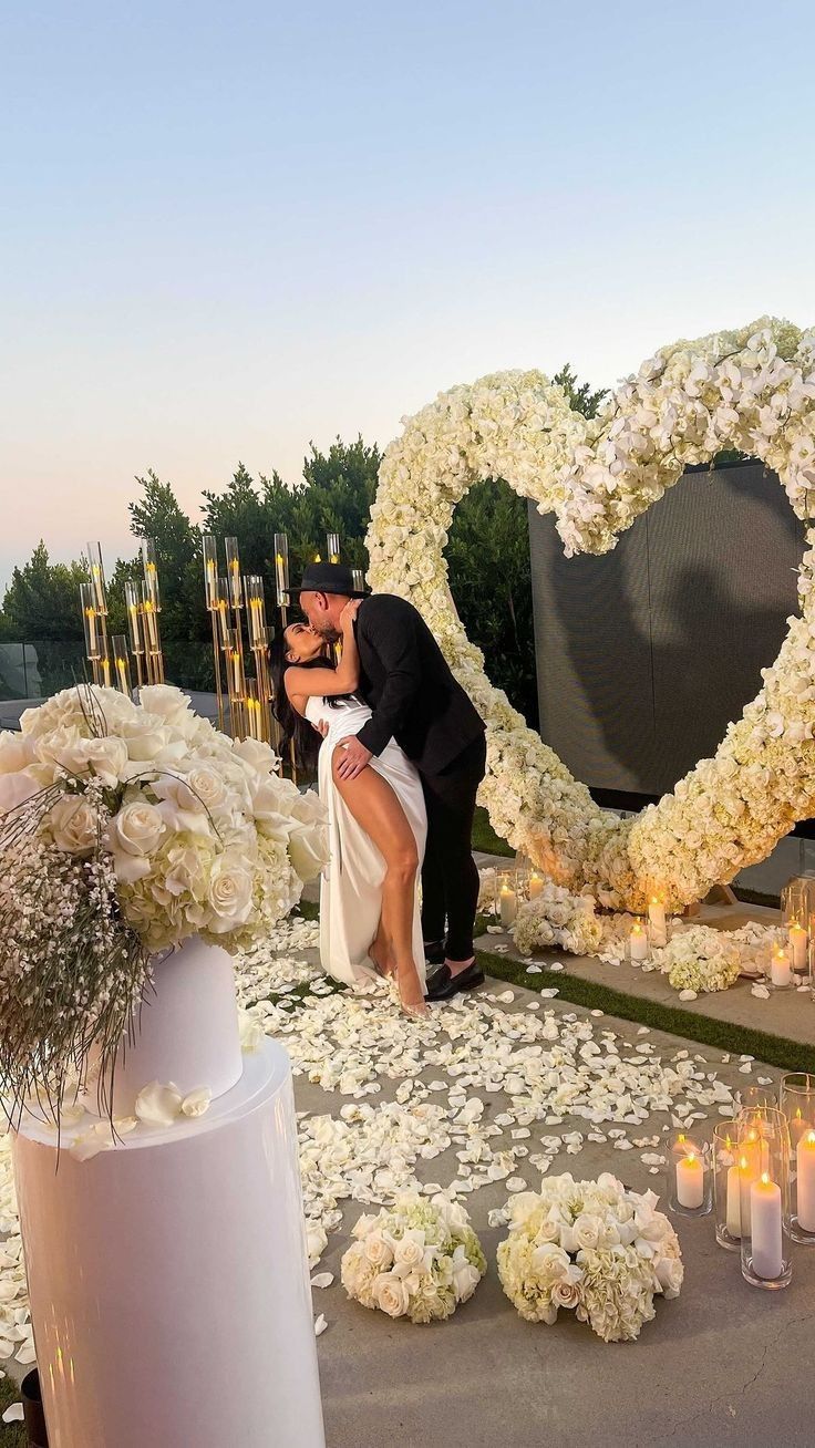 a newly married couple kissing in front of a heart - shaped floral arrangement