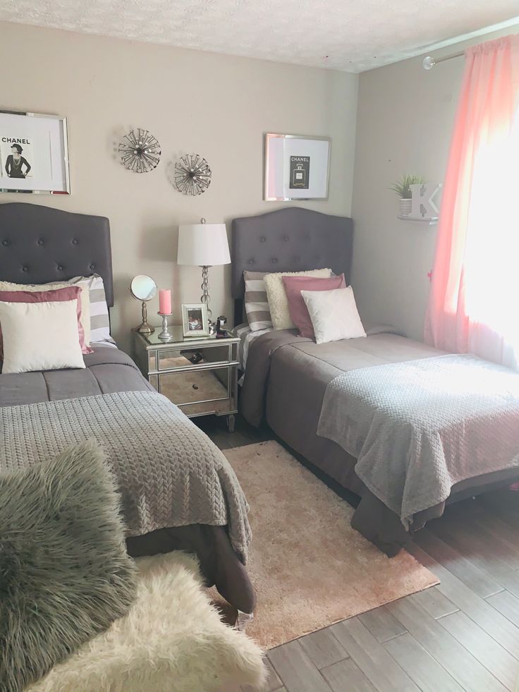 two beds in a bedroom with gray and white bedding, pink drapes, and pictures on the wall