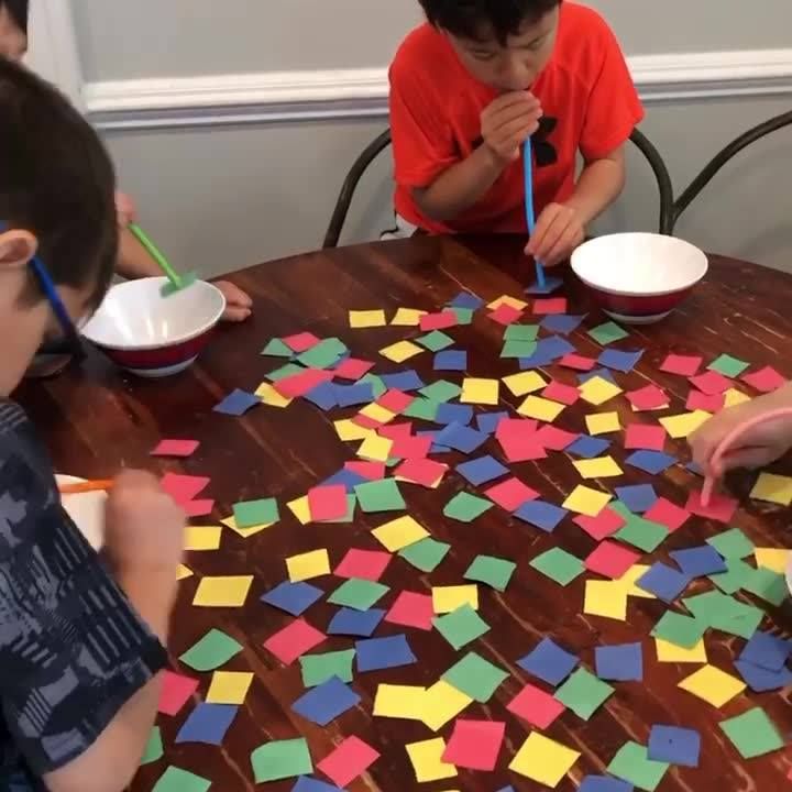 two boys are sitting at a table with colored paper on it and one boy is holding a toothbrush