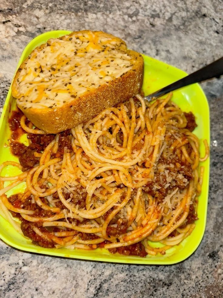 a yellow plate with spaghetti and bread on it, sitting on a granite counter top