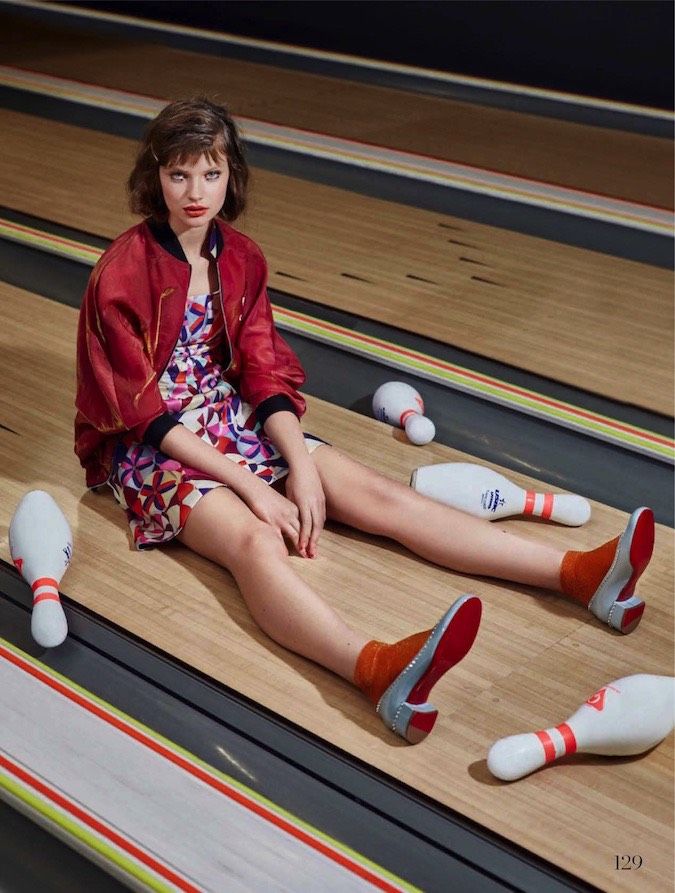 a woman sitting on top of a bowling alley with her feet up in the air