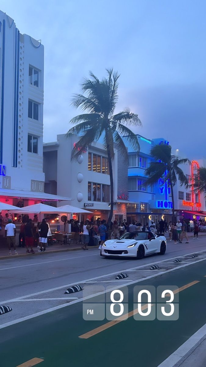 a white car parked on the side of a road next to tall buildings and palm trees