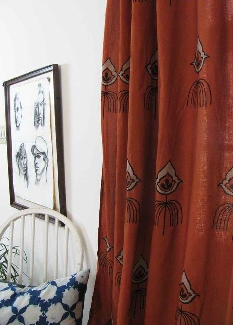 an orange curtain with black and white drawings on it next to a chair in front of a window