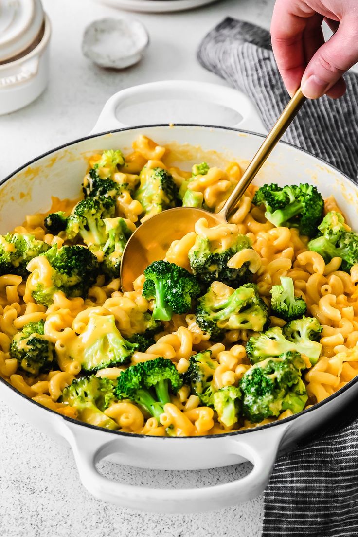 a person is stirring broccoli and noodles in a skillet