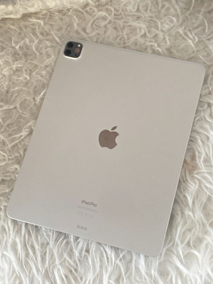 an apple ipad sitting on top of a fluffy white blanket next to a cell phone