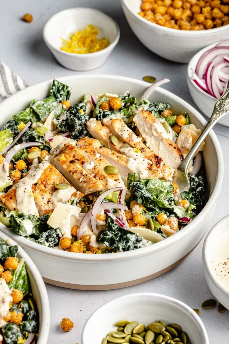 kale caesar salad with chicken and carrots in white bowls on a counter top