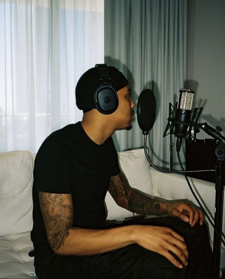 a man with headphones sitting on a couch in front of a microphone and recording equipment