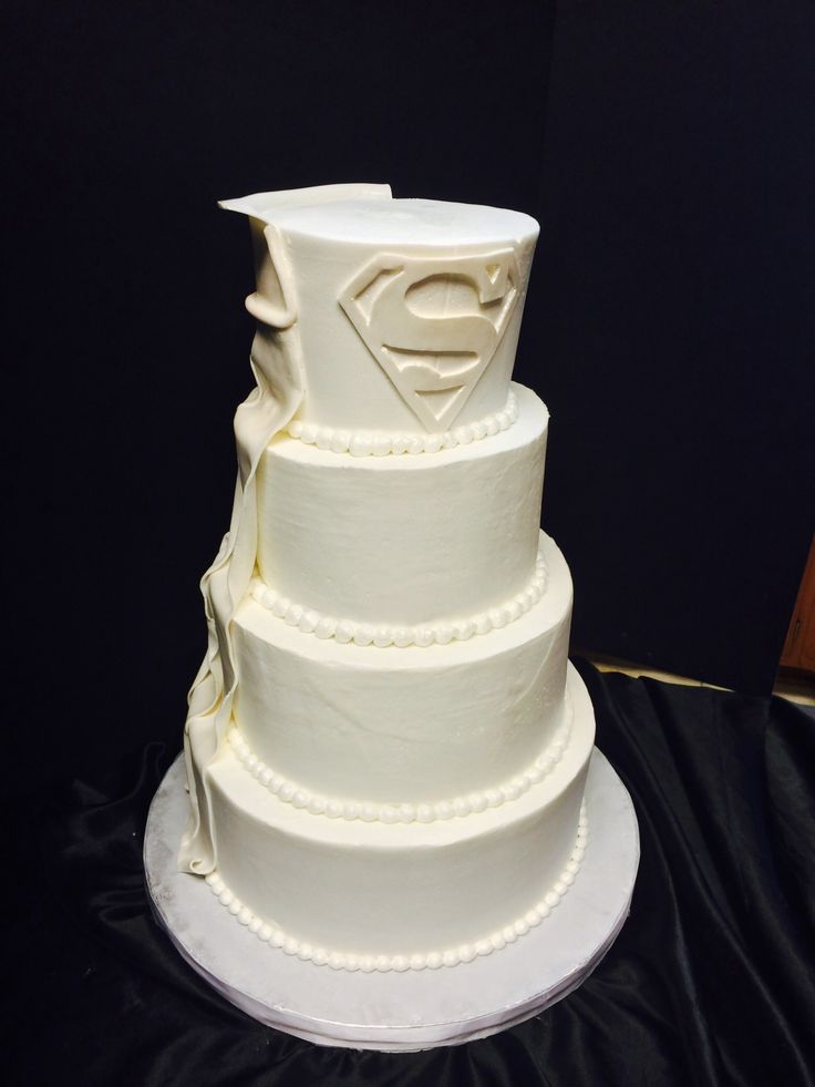 a three tiered white cake with a superman symbol on top