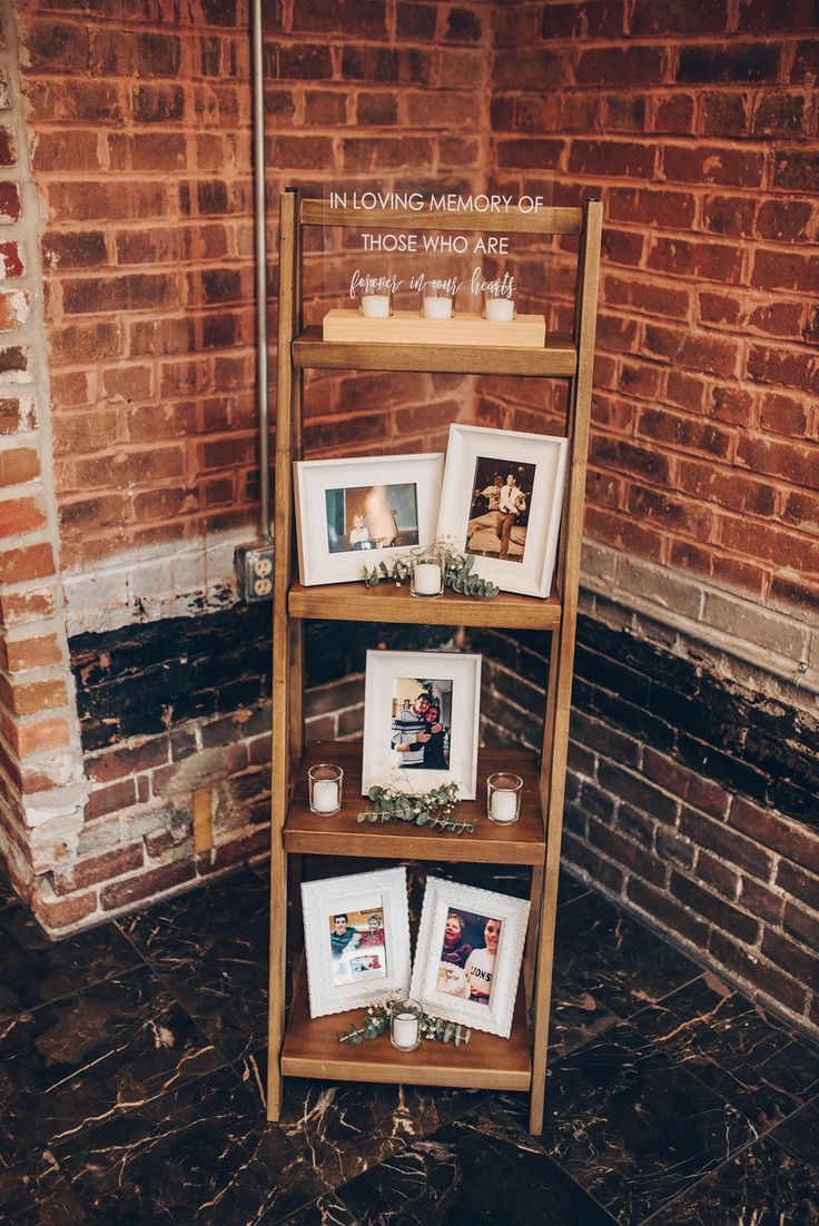 a wooden shelf with pictures and candles on it in front of a brick wall that says,