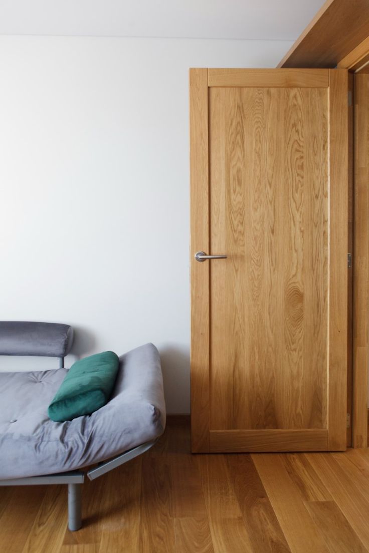 a bed sitting next to a wooden door in a white room with hardwood flooring