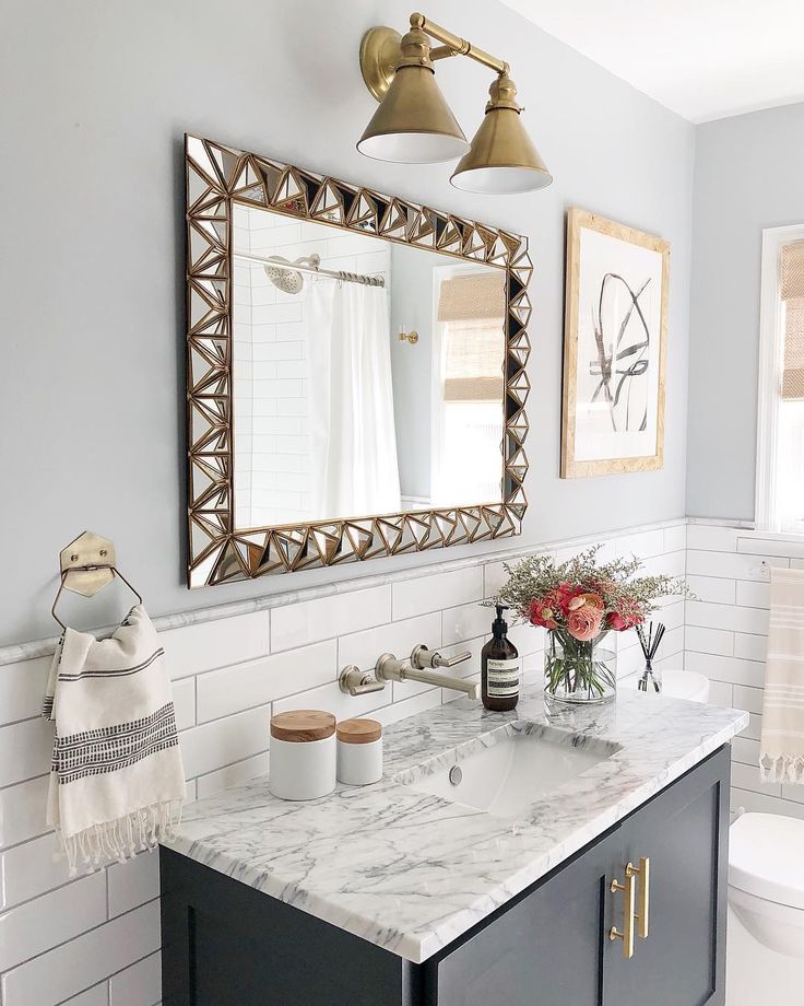 a bathroom with marble counter tops and gold accents on the mirror above it is a white toilet