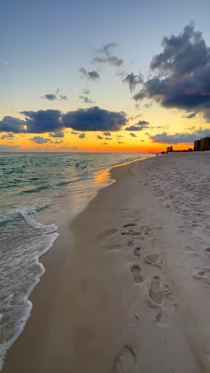 footprints in the sand at sunset on an empty beach with waves coming in to shore