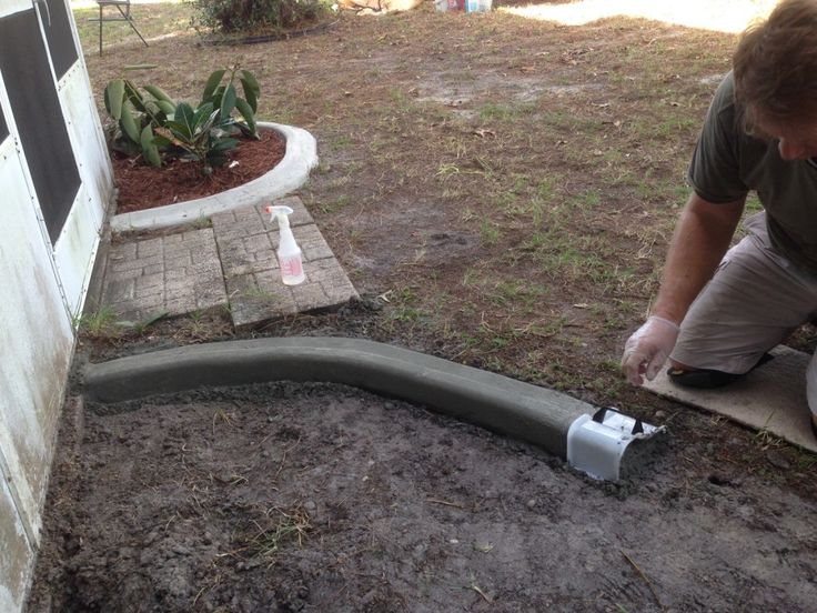 a man is working on a pipe in the ground next to a wall and some plants