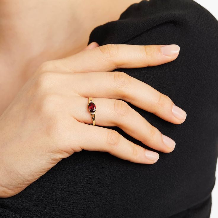 a woman's hand with a gold ring and a red stone on her finger