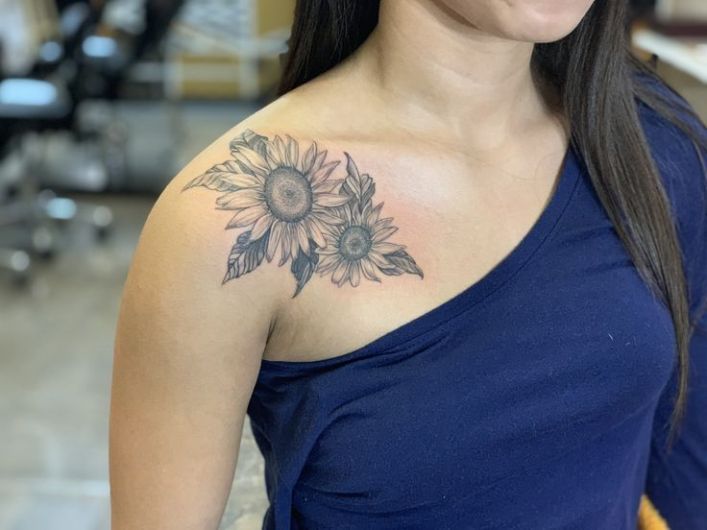 a woman with a sunflower tattoo on her chest and shoulder is smiling at the camera