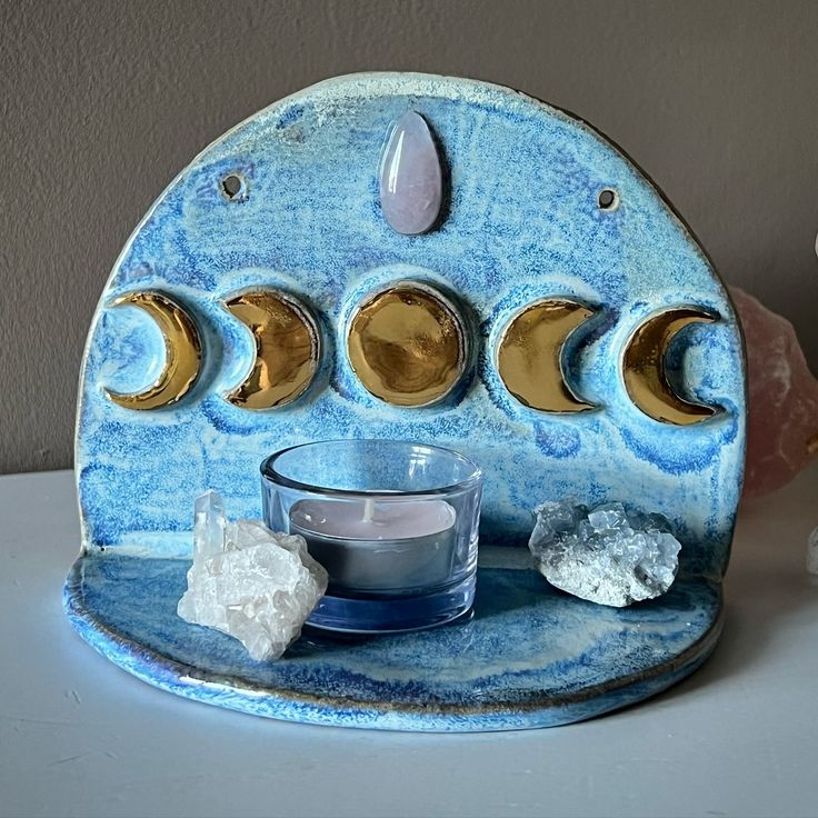 a blue and gold plate with three moon phases on it next to a candle holder