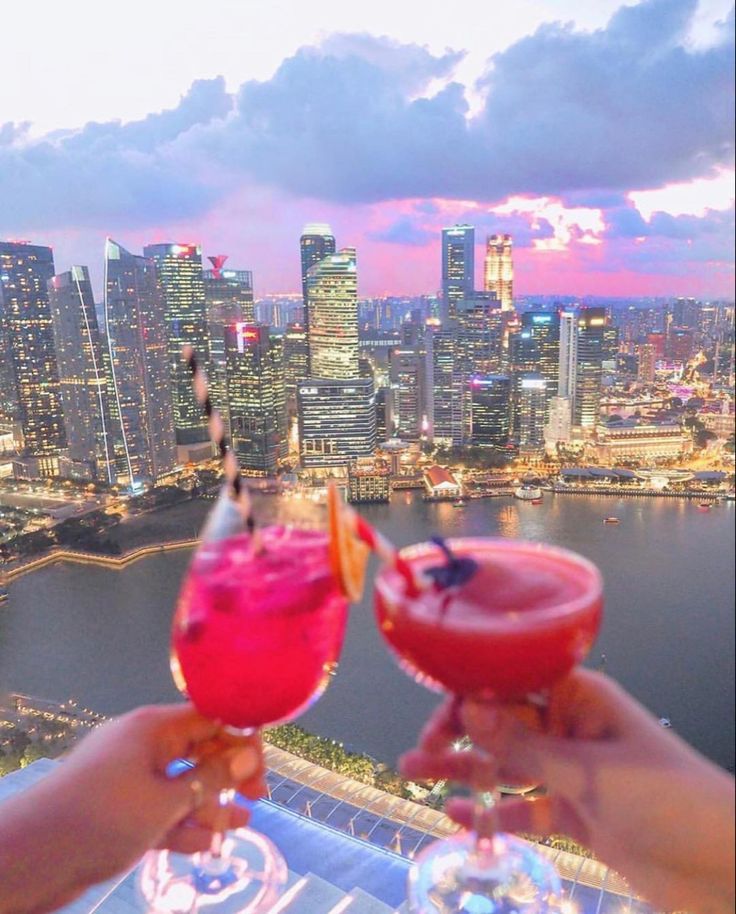 two people holding up wine glasses in front of a cityscape