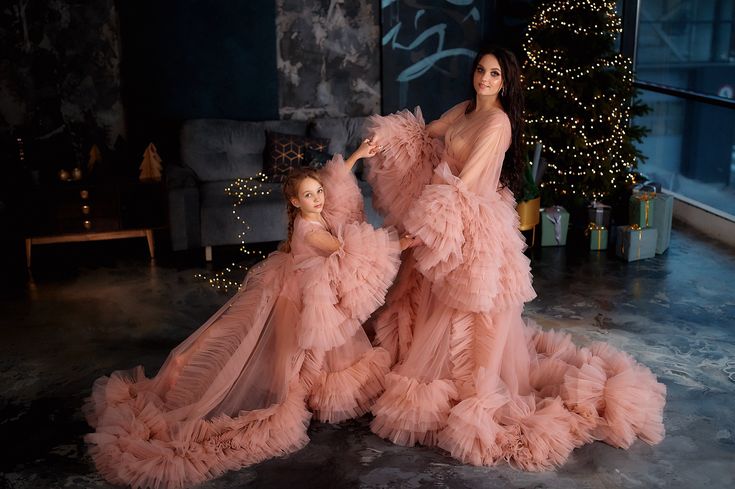 two women in pink gowns standing next to each other near a christmas tree with lights on it