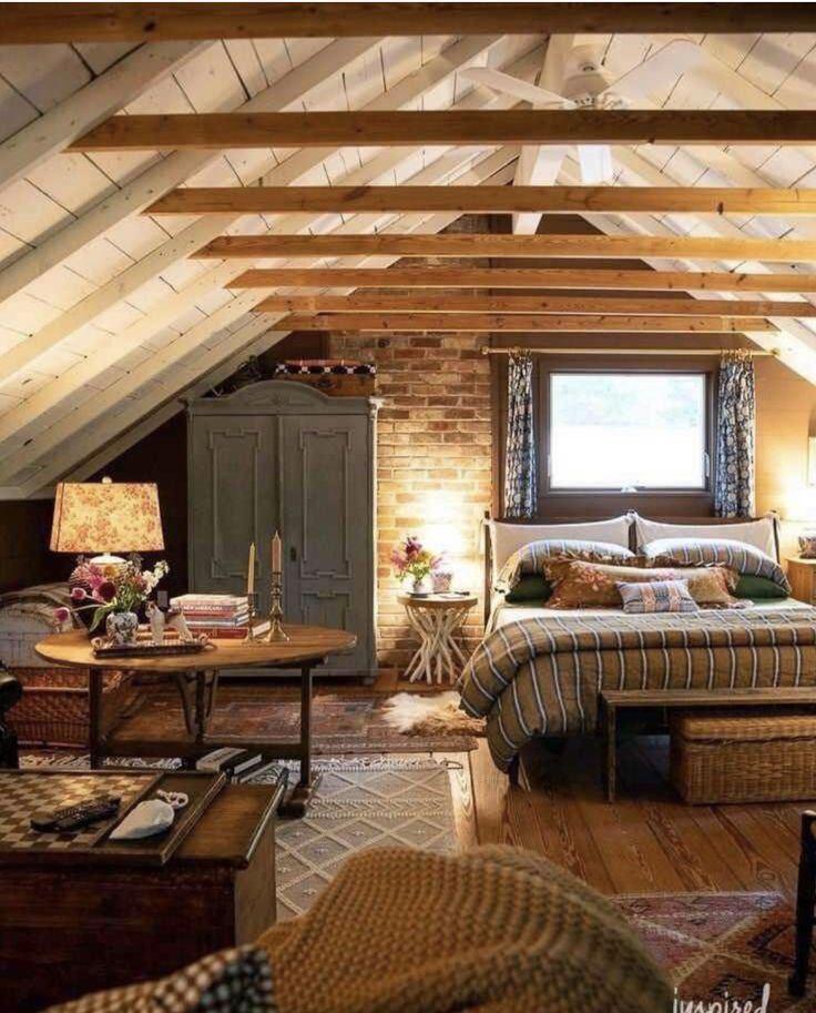 an attic bedroom with exposed wood beams and brick walls is furnished with wicker furniture