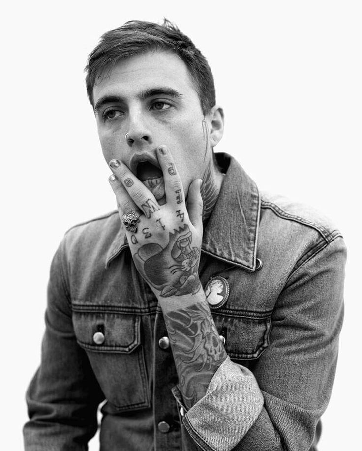 a man with tattoos holding his hands up to his mouth and making a face while wearing a denim jacket