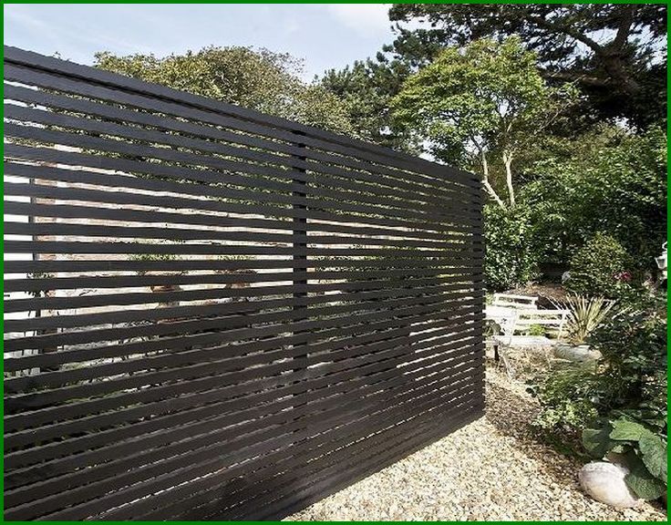 a wooden fence in the middle of a gravel area with trees and bushes behind it