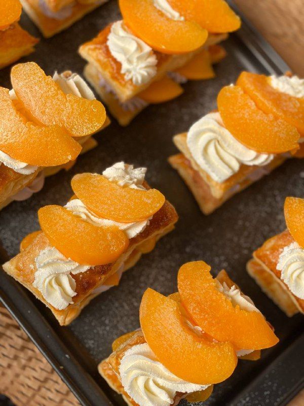 small desserts with orange slices and whipped cream toppings on a baking sheet, ready to be eaten