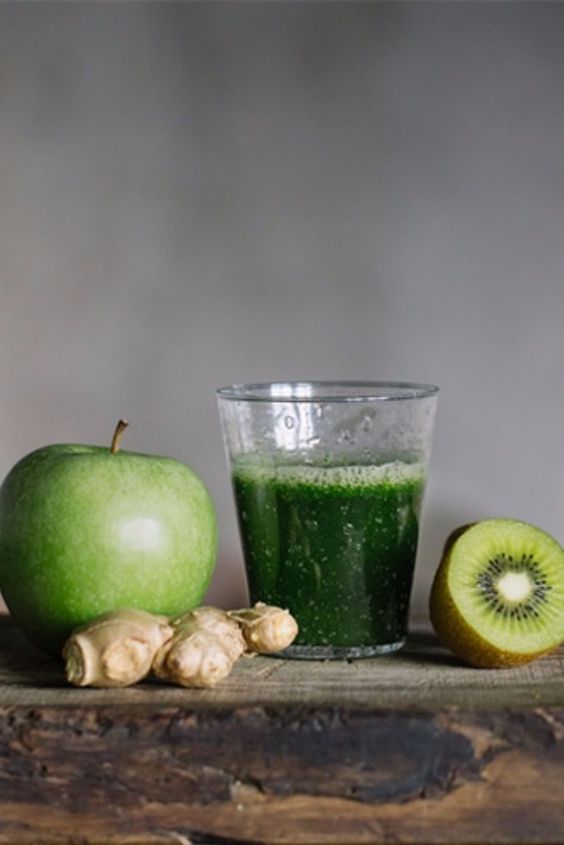 an apple, kiwi and ginger sit on a table next to a glass of green juice