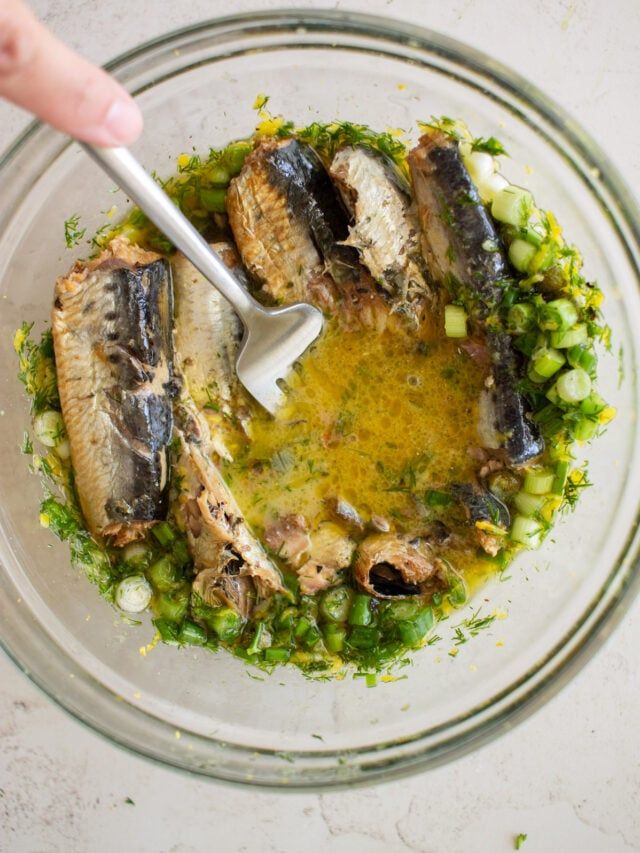 a bowl filled with fish and vegetables on top of a white countertop next to a person's hand holding a fork