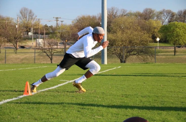 a man running across a lush green field next to an orange cone on top of a football field