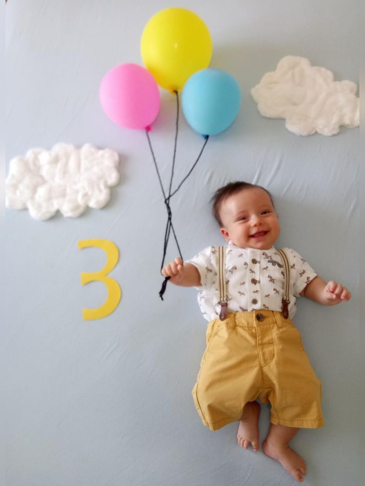 a baby is laying down with balloons on the wall