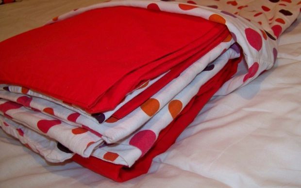 three folded blankets on top of each other on a bed with white sheets and polka dots