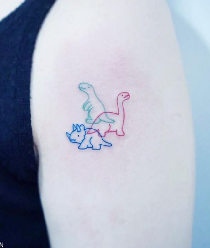 a woman's arm with a small dinosaur and cat tattoo on the left shoulder